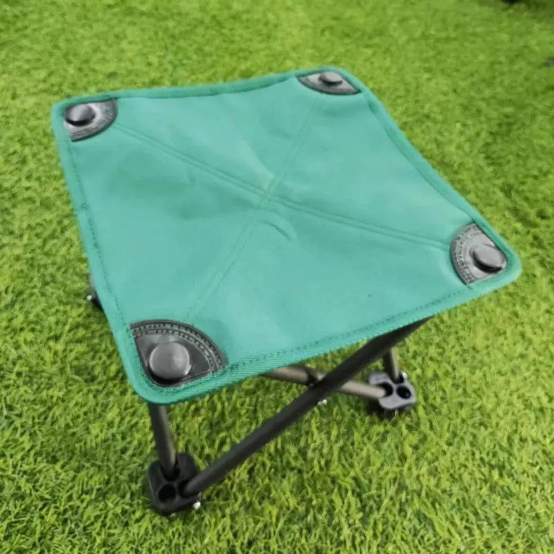 Teal folding stool with metal legs on a grassy background