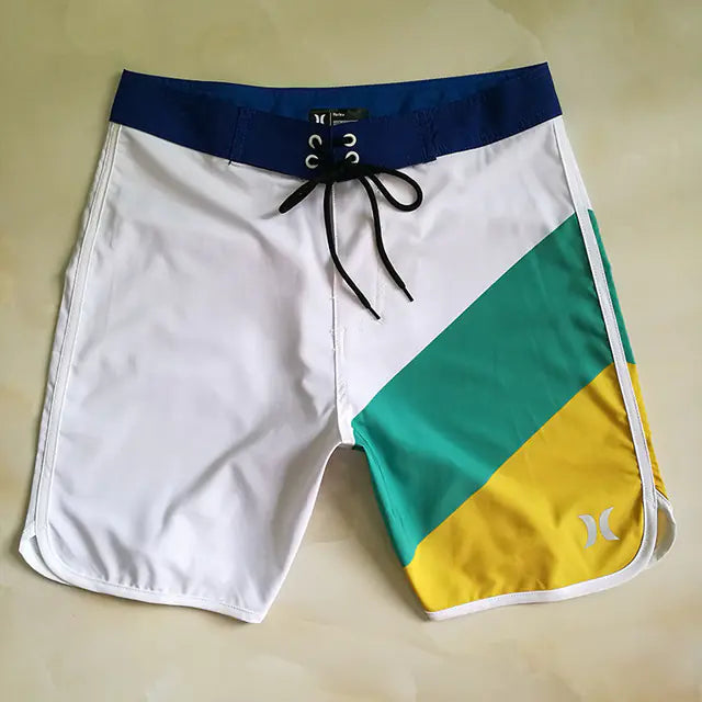 Color-blocked board shorts with white, green, and yellow sections on a beige background