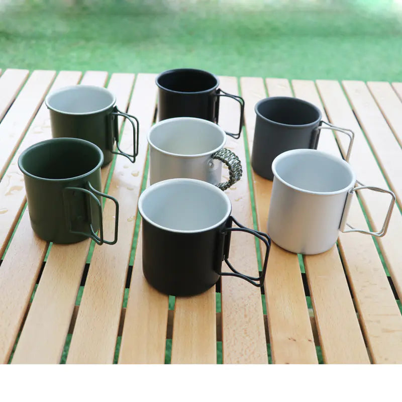 Set of eight mugs in black, gray, and green on a wooden surface with a blurred green background.
