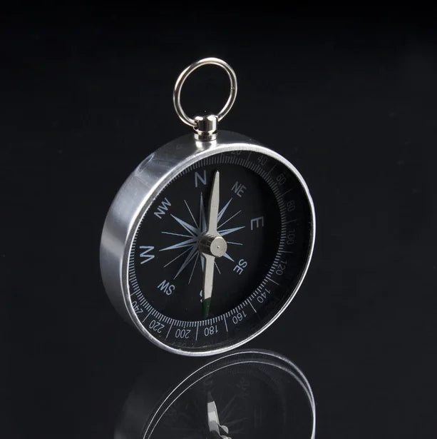 Compass with black dial and silver casing on a reflective surface with a dark background