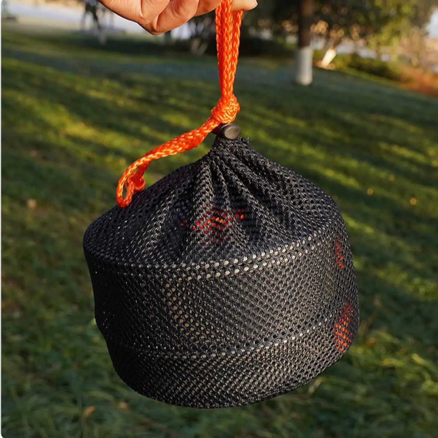 Black woven drawstring bag with orange rope handle held by a hand on grass