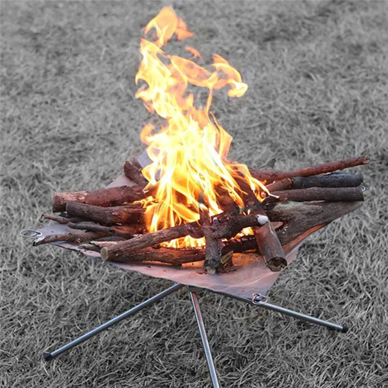Small campfire with flames burning on a metal fire pit on grass.