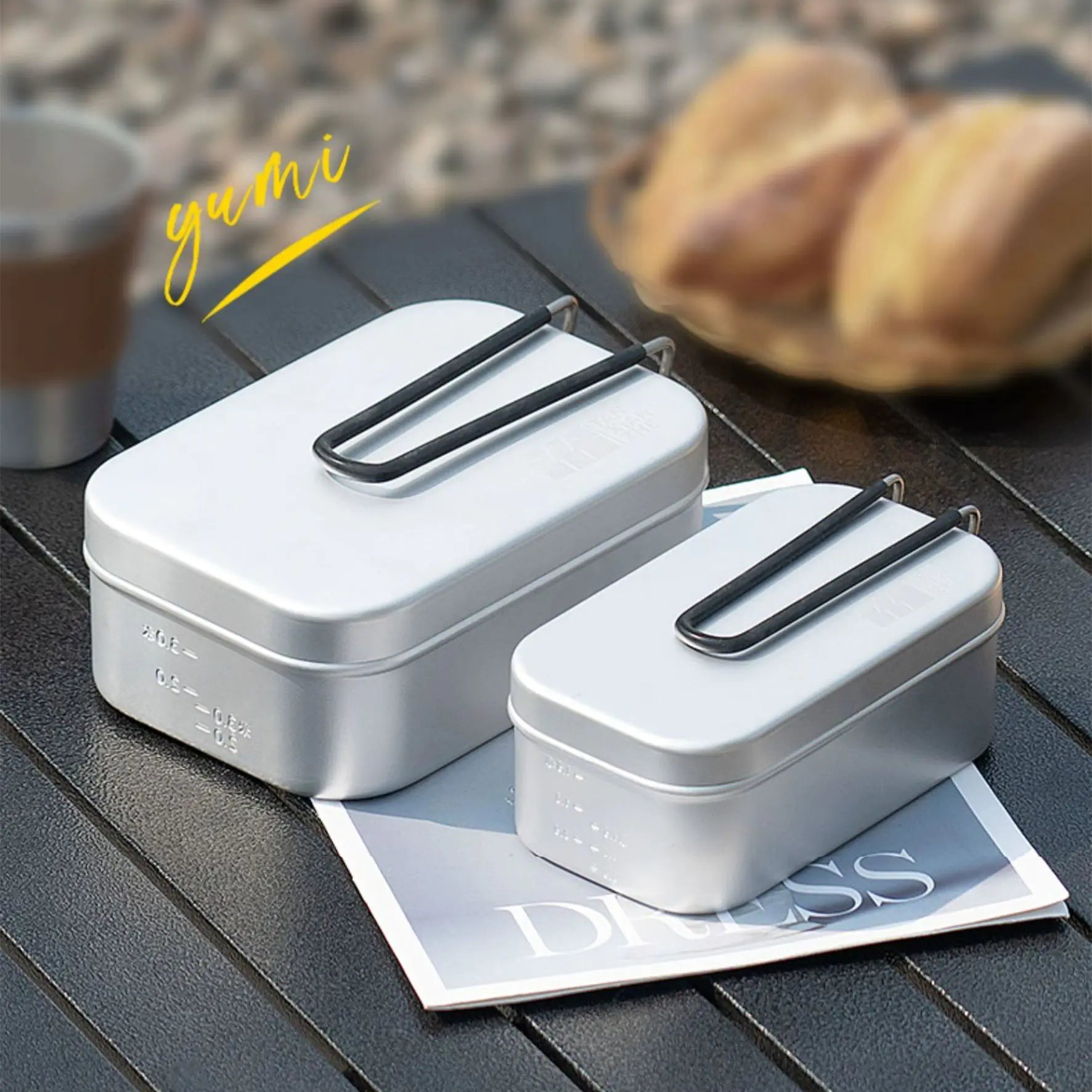 Two white lunch boxes with black handles on a wooden surface with a blurred background.