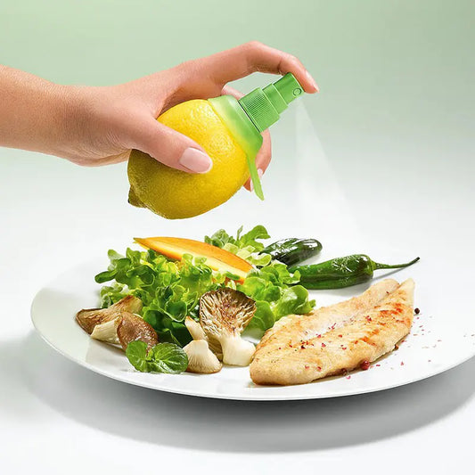 Hand holding a real lemon that has a screwed in spray pump so you can spray juice directly from the fruit. Positioned over a plate of grilled fish and a green salad