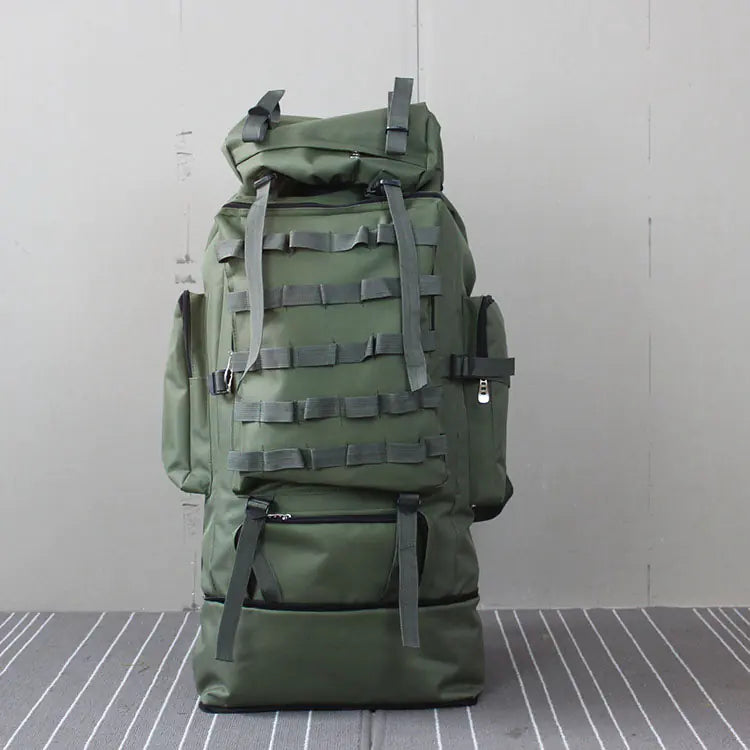 Green military-style backpack on a gray floor with a white wall background