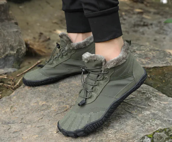 Green winter waterproof hiking shoes with fur lining worn by a person on a stone surface.