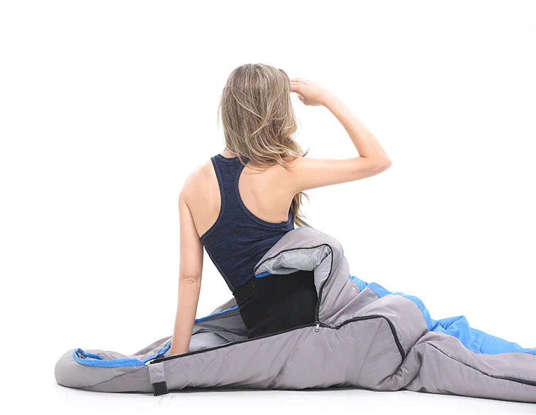 Woman sitting on a gray sleeping bag with blue interior on a white background