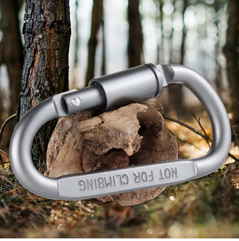 Metal carabiner attached to a tree with 'Not for Climbing' text in a forest setting