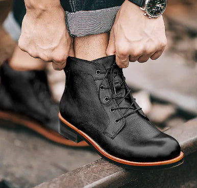 Person adjusting black leather men's ankle laceup boots with a blurred background