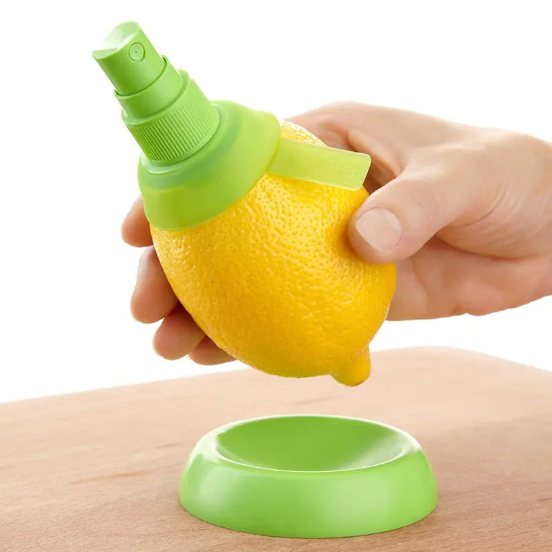 Hand holding a real lemon that has a screwed in spray pump so you can spray juice directly from the fruit. Positioned over a small green holder on a wood table