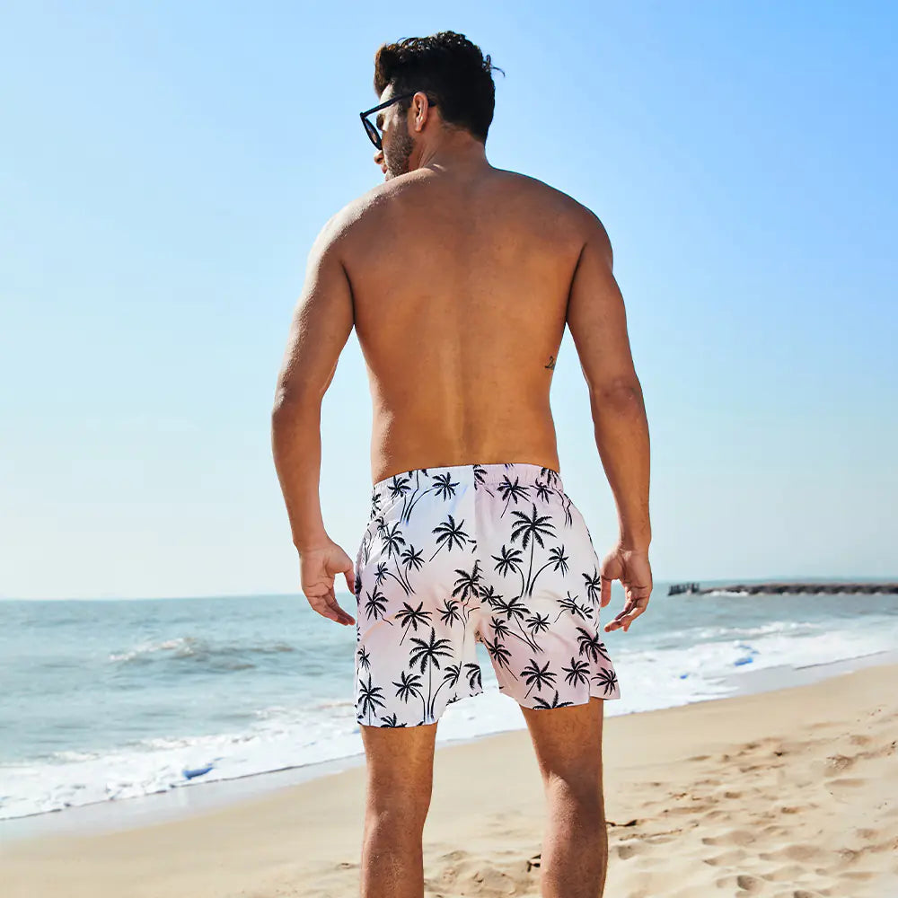 Man wearing palm tree patterned shorts standing on a beach.